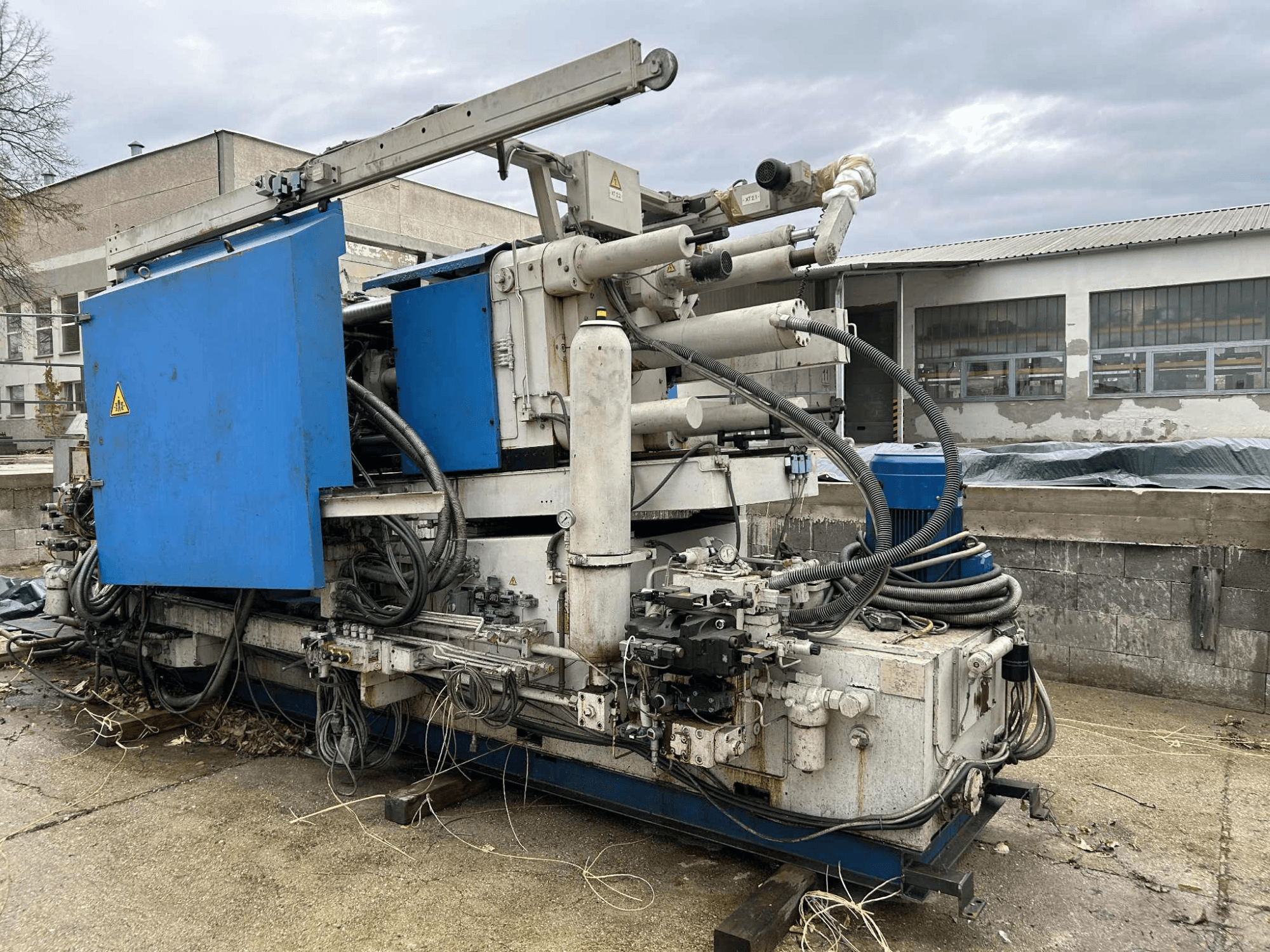 Велика промислова гідравлічна машина з синім корпусом, різноманітними шлангами та металевими компонентами, вид збоку.