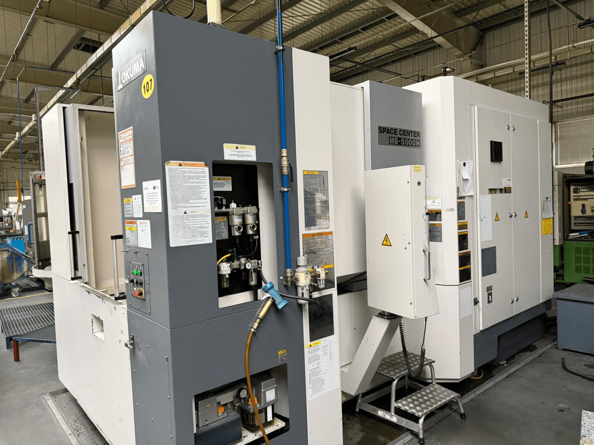Горизонтальний обробний центр Okuma MB 5000H, вид збоку, що демонструє панель керування та компоненти верстата в заводських умовах.