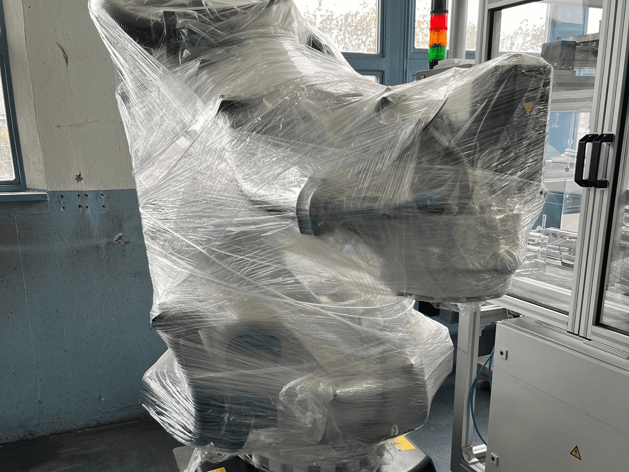 Промисловий роботизований маніпулятор в пластиковій оболонці, вигляд спереду. Включає блок управління та індикаторну лампу. Бренд не видно.