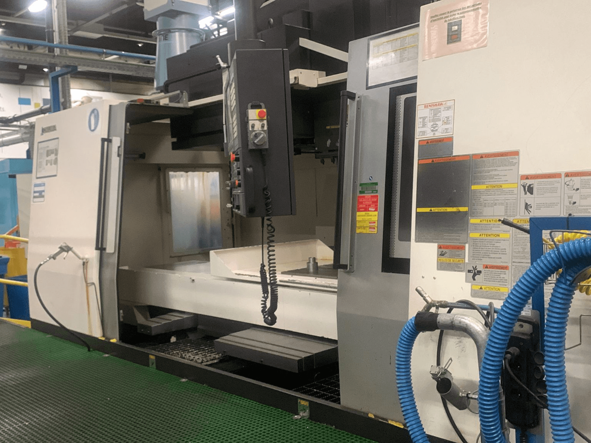 Вертикальний обробний центр Okuma Millac 852 VII, вид спереду, на якому видно панель управління, зону шпинделя та попереджувальні наклейки.