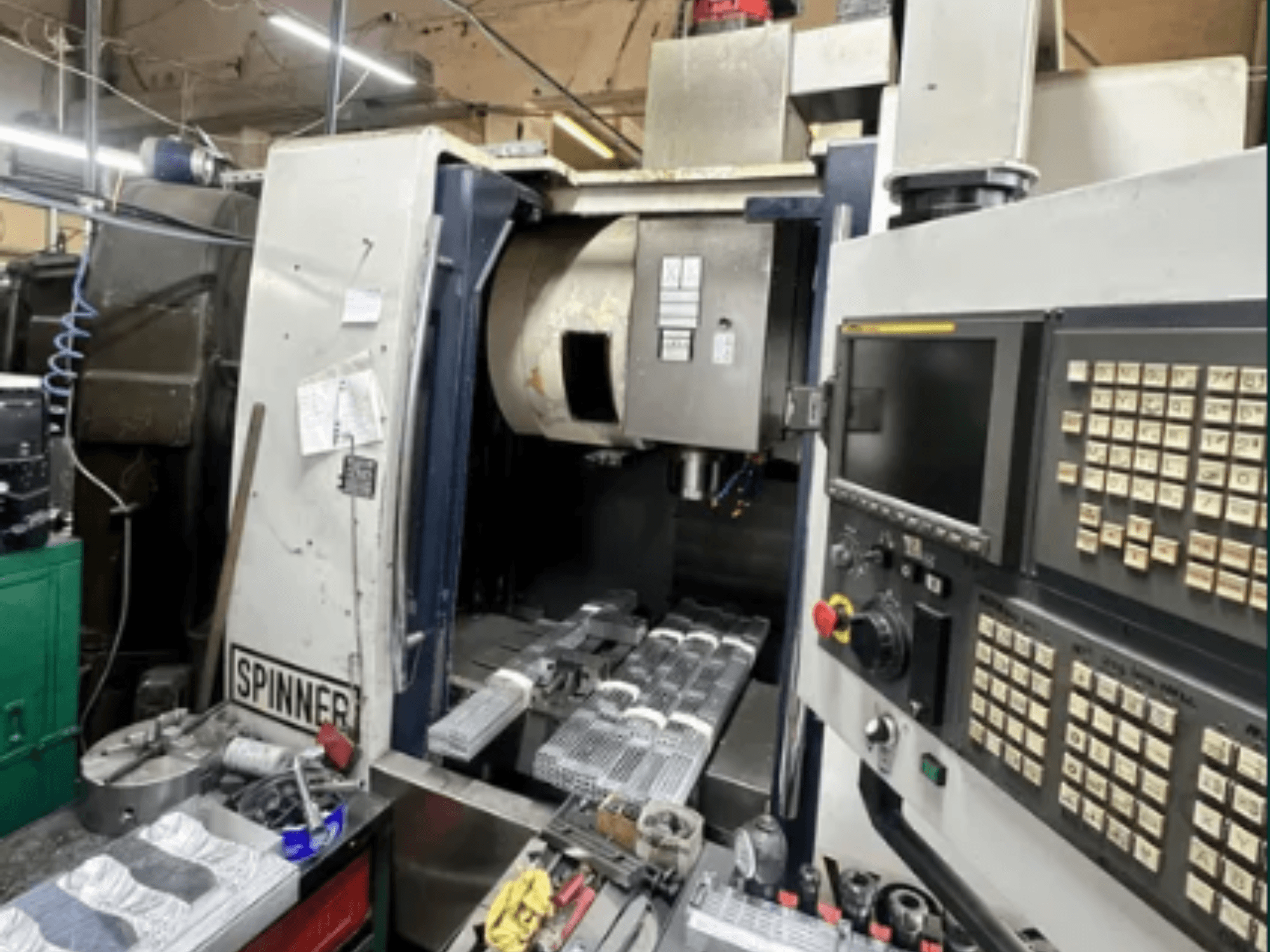 Верстат з ЧПУ від Spinner, вигляд спереду; має сенсорний інтерфейс, інструменти на робочій поверхні та оброблені деталі, готові до обробки.
