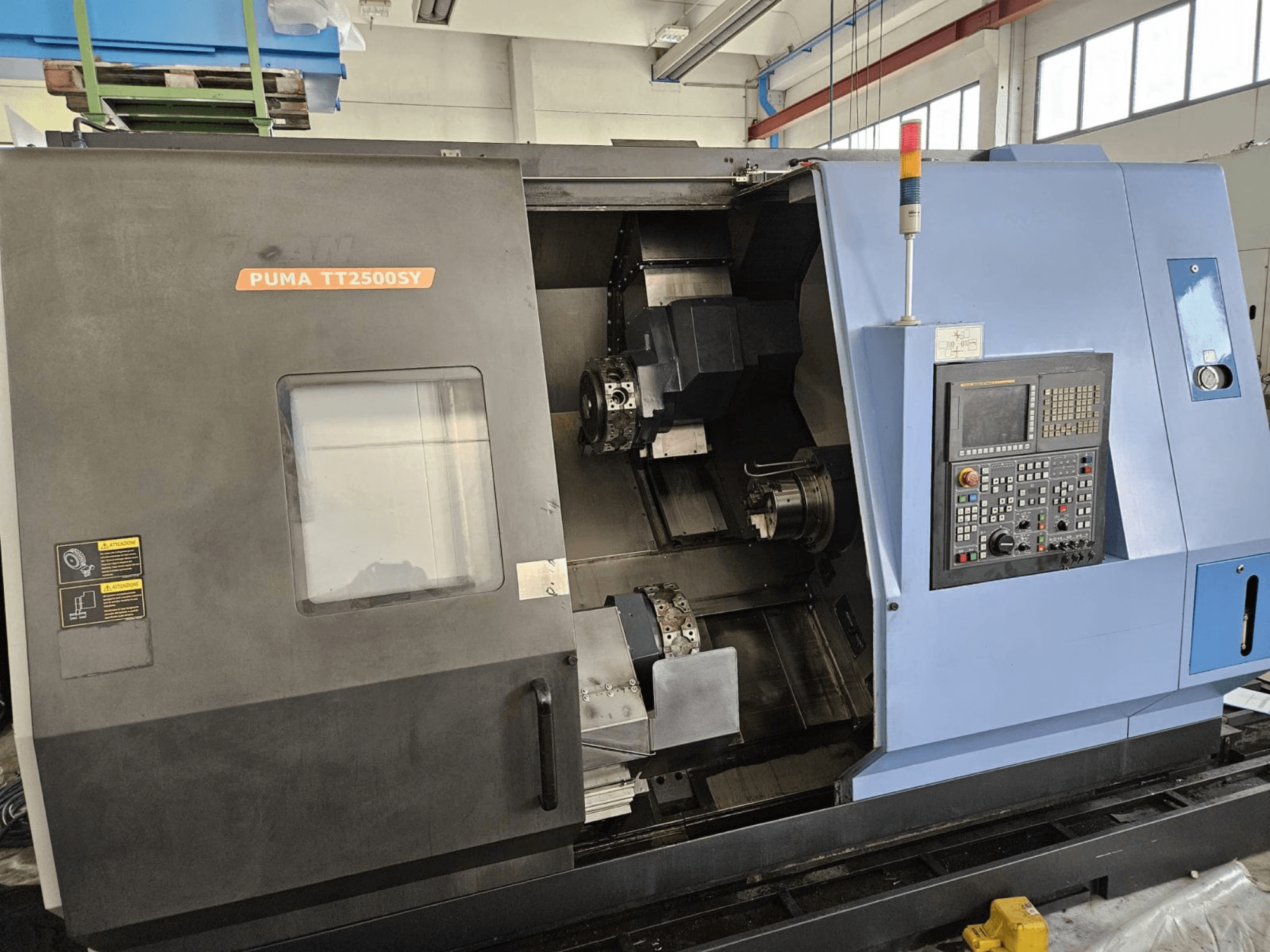 Багатошпиндельний токарний верстат DOOSAN PUMA TT2500SY, вид спереду, на якому видно панель управління та деталі внутрішньої частини верстата.