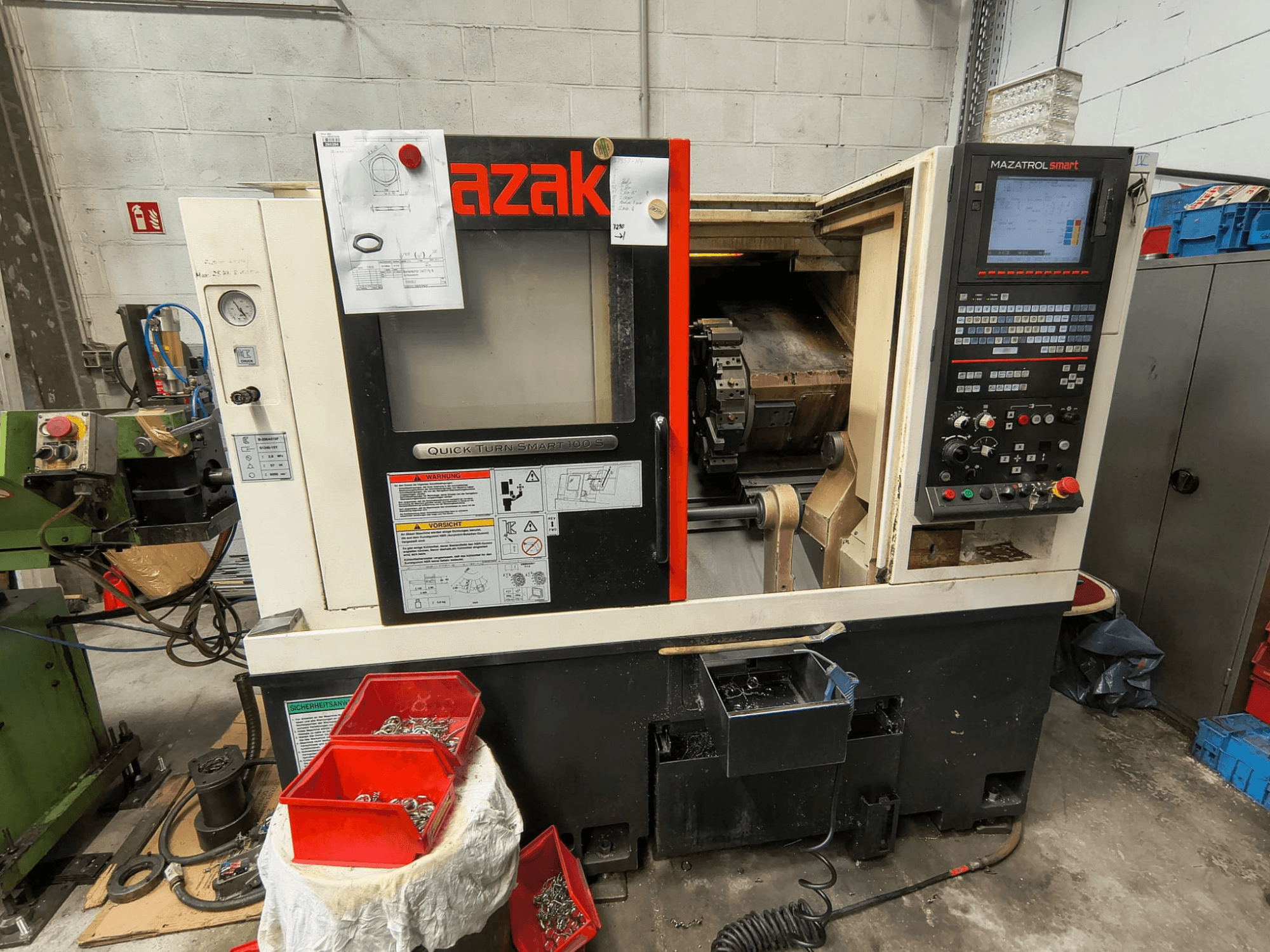 Mazak Quick Turn Smart 100 S, вид збоку, на якому видно панель керування, піддон для охолоджувальної рідини та контейнери для зберігання гвинтів.