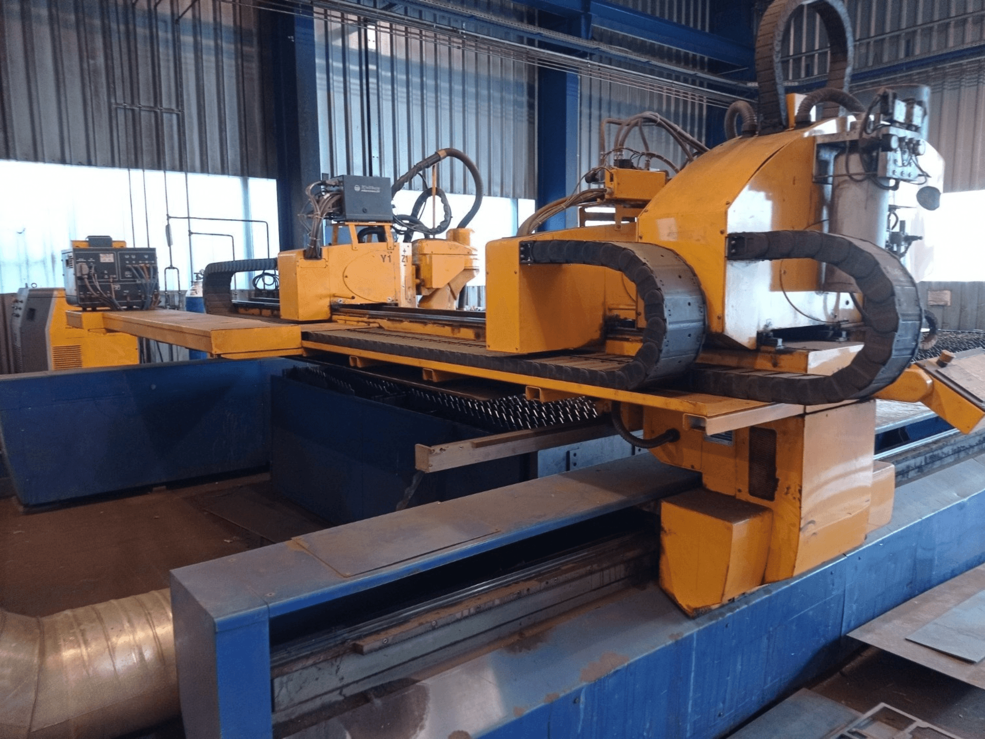 Жовтий верстат для плазмового різання з ЧПУ з двома горизонтальними рукавами, показаний спереду, з панеллю керування та робочим столом.