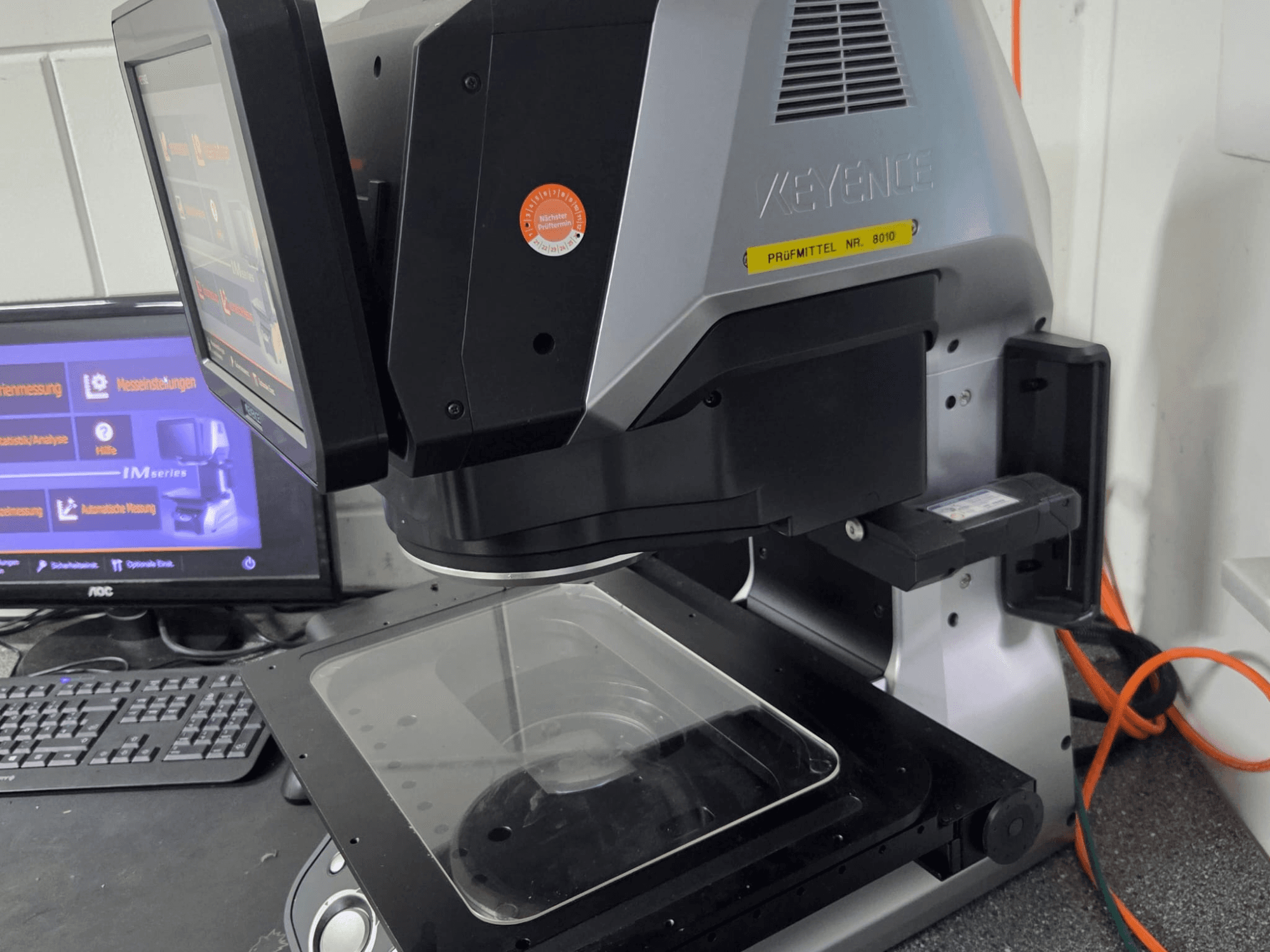 Оптична вимірювальна машина KEYENCE IM 7030, вигляд спереду з сенсорним дисплеєм і скляною вимірювальною пластиною.