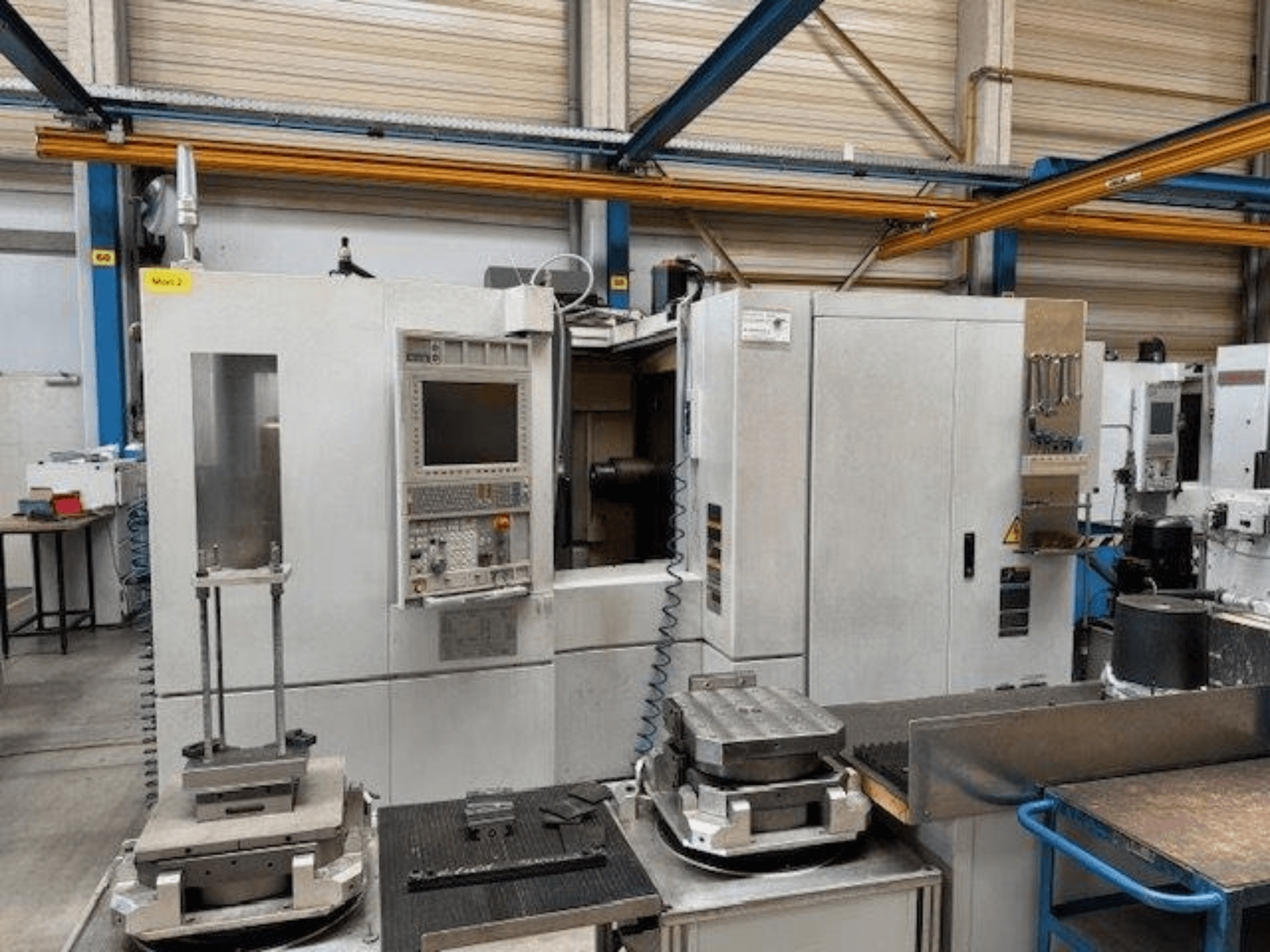 MORI SEIKI NH4000 DCG - вид спереду горизонтального обробного центру з панеллю керування та заготовками на столі.