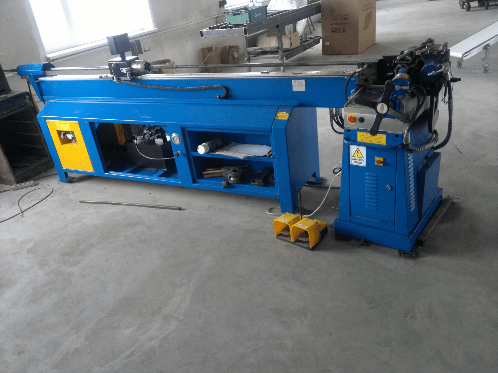 Синій деревообробний верстат з жовтими акцентами, вид збоку; оснащений панеллю керування, ножними педалями та обертовим ножем.