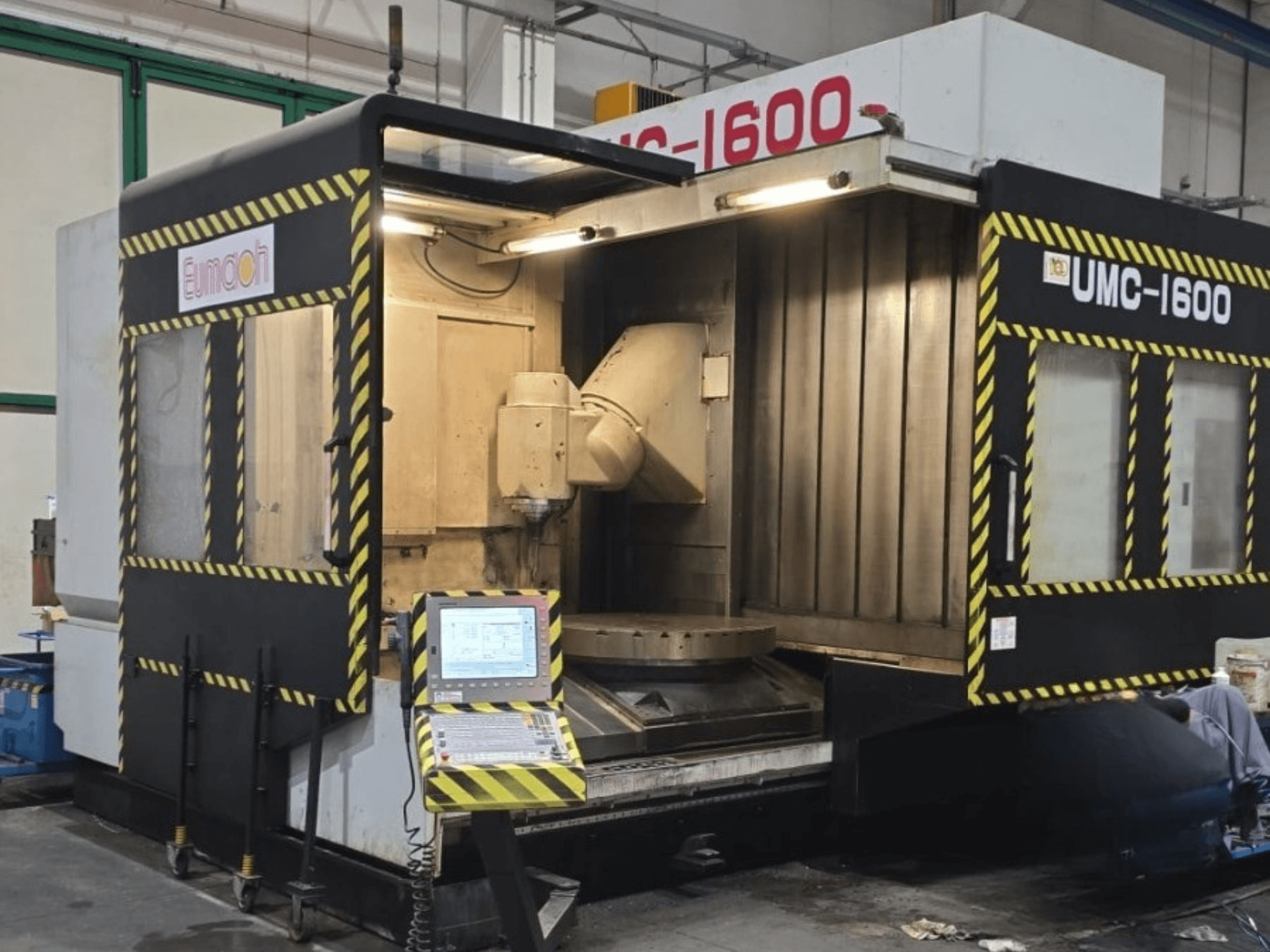 Вертикальний обробний центр Eumach UMC-1600, вид спереду, на якому видно органи управління та зону обробки з позначками безпеки.