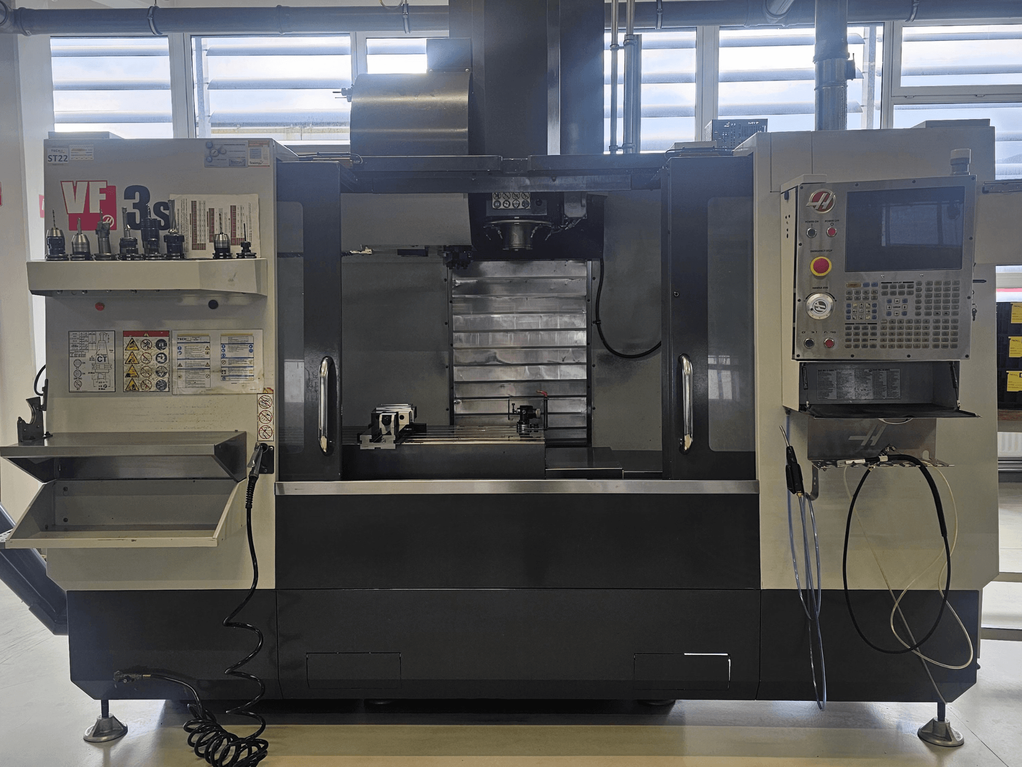 Фрезерний верстат з ЧПК Haas VF3SS, вид спереду, з тримачами інструментів, панеллю керування та порожнім піддоном для ЗОР, з видимими етикетками безпеки.