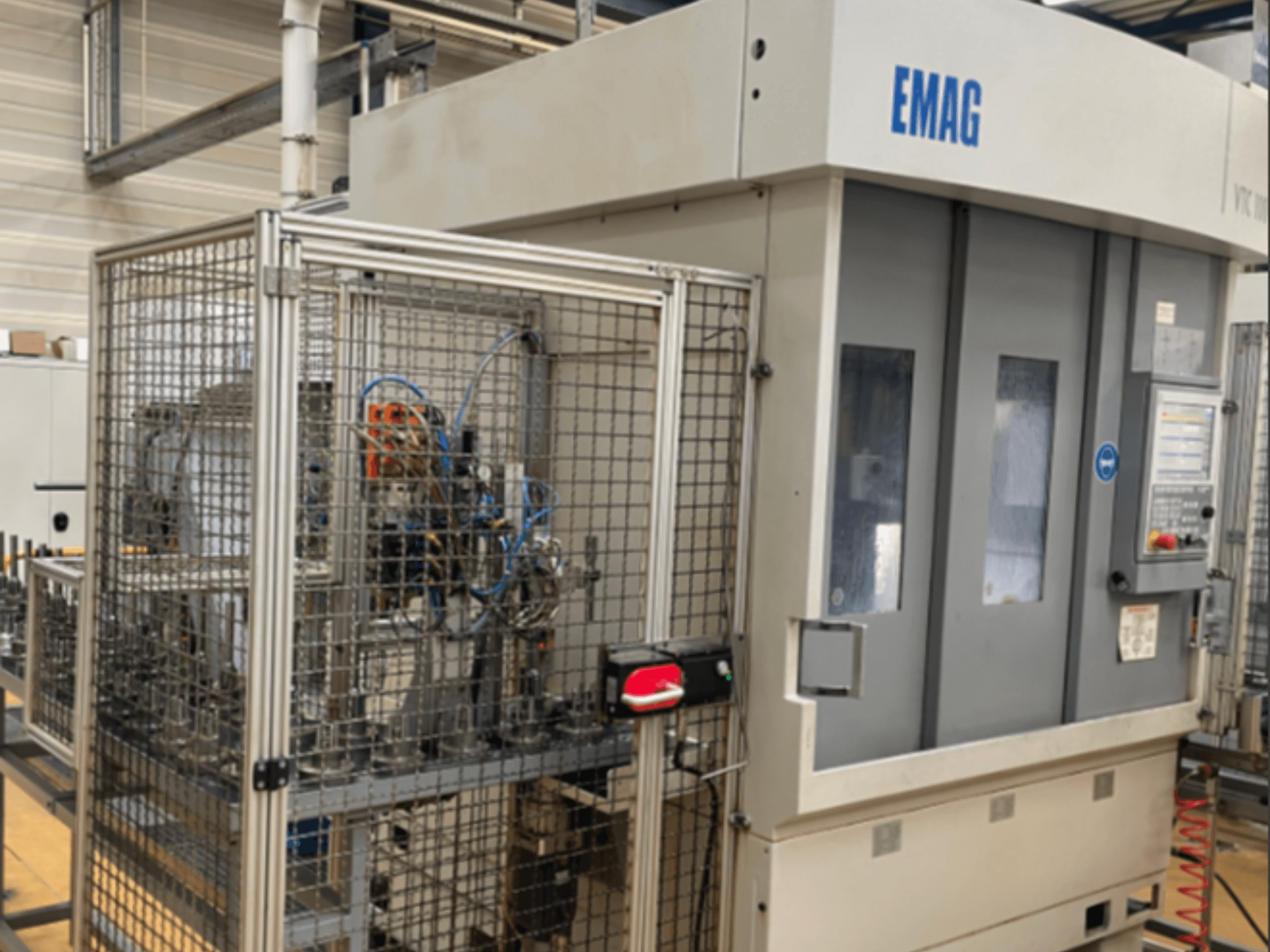 Вертикальний токарний верстат EMAG VTC 100 у боковому ракурсі, на якому видно панель управління та деталі захисних огорож.