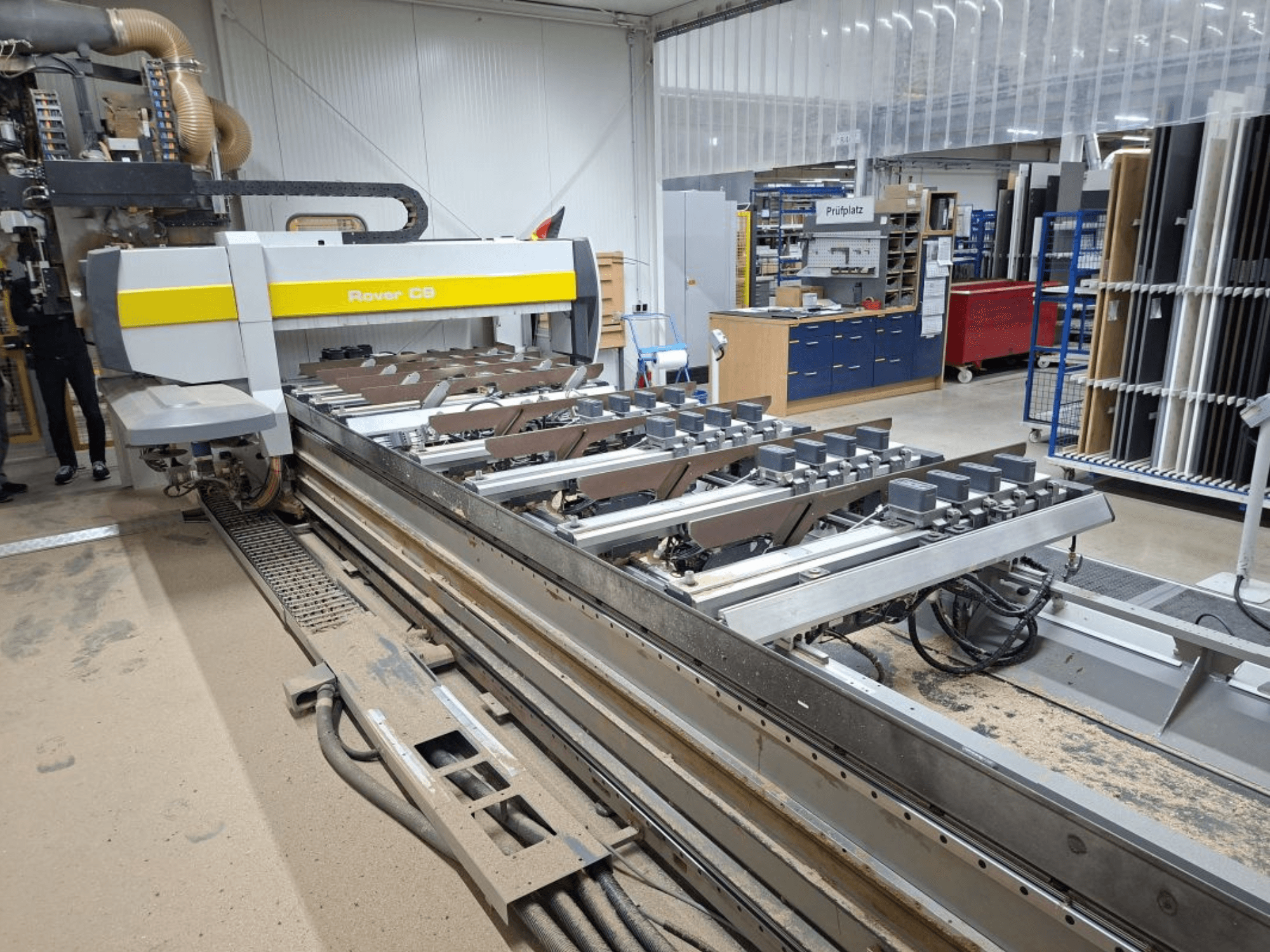 Верстат з ЧПК Rover C9 у майстерні; вид спереду - ріжучі інструменти та конвеєрна система, на підлозі скупчення пилу.