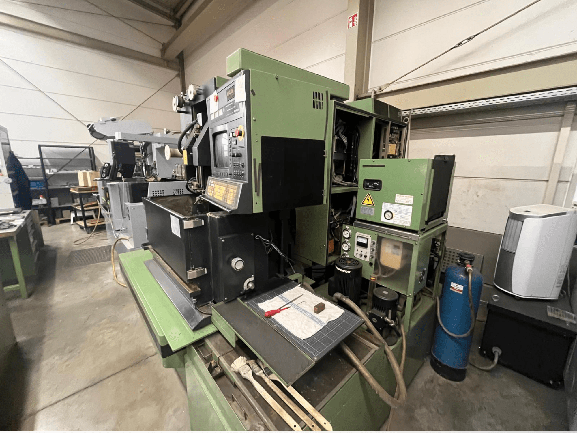 Зелена промислова машина з панеллю керування, вид збоку; включає гідравлічні компоненти та робочу поверхню з інструментами.