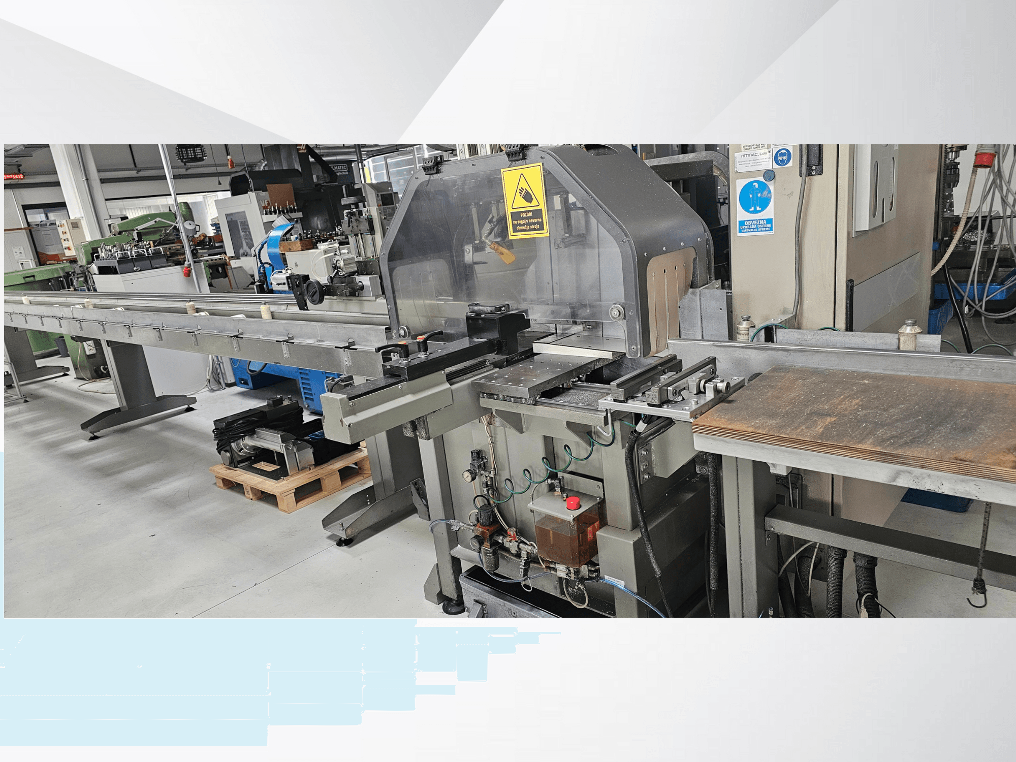 Промисловий розкрійний верстат збоку, з довгим конвеєром, панеллю керування та попередженнями про безпеку.