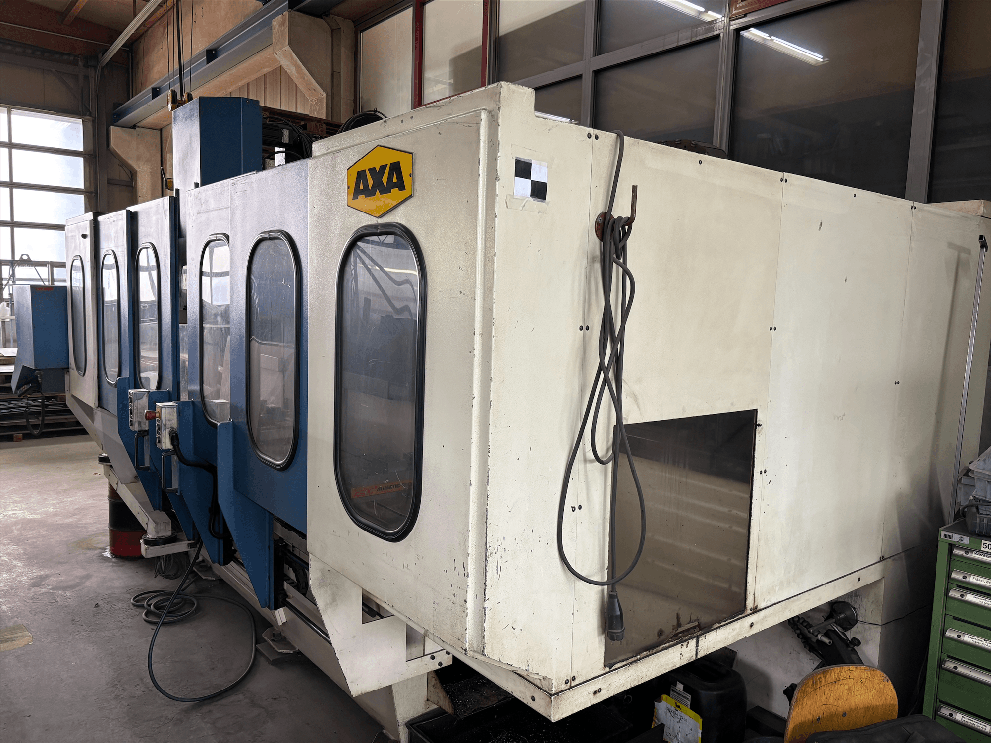 Вертикальний обробний центр AXA VSC-1-M/C, вигляд спереду, з великою білою шафою та синьою панеллю керування.