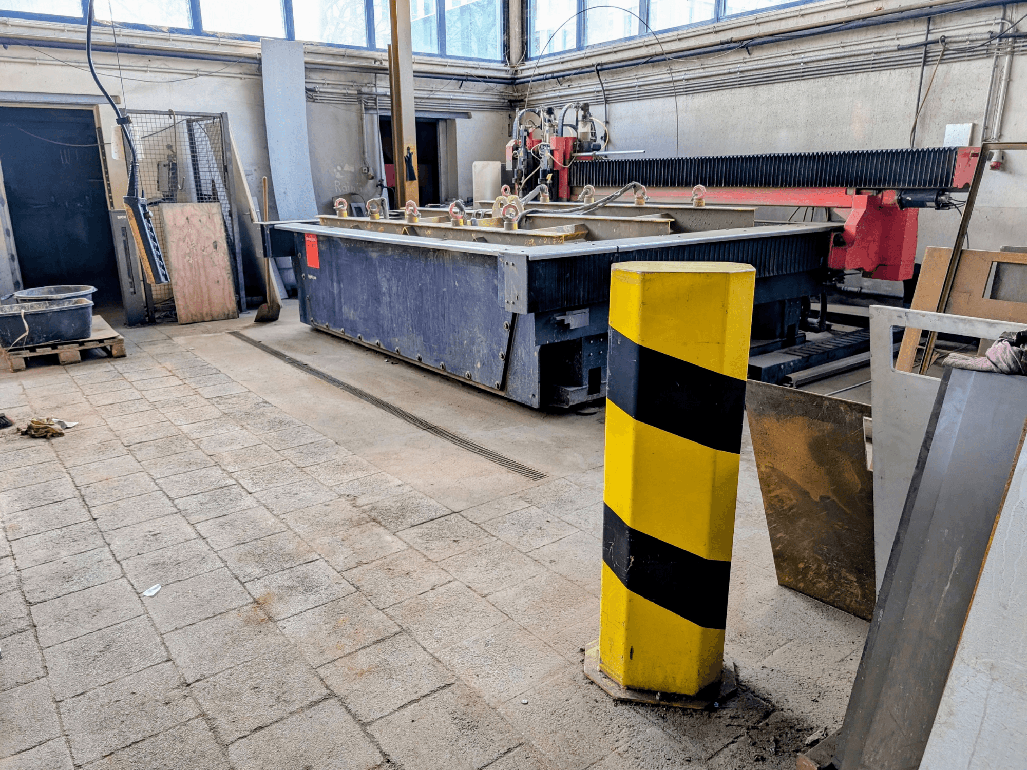 Машина гідроабразивного різання Bystronic Byjet L 2030 в майстерні, вид збоку, з жовтим захисним стовпом і навколишніми матеріалами.