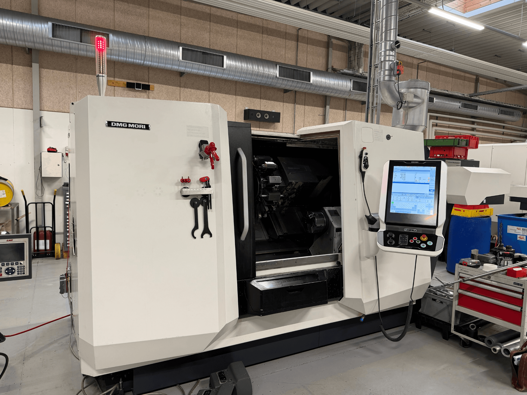 Горизонтальний токарний верстат DMG MORI CLX 450 V6, вид спереду, на якому видно панель управління, кнопку аварійної зупинки та сигнальну лампу безпеки.