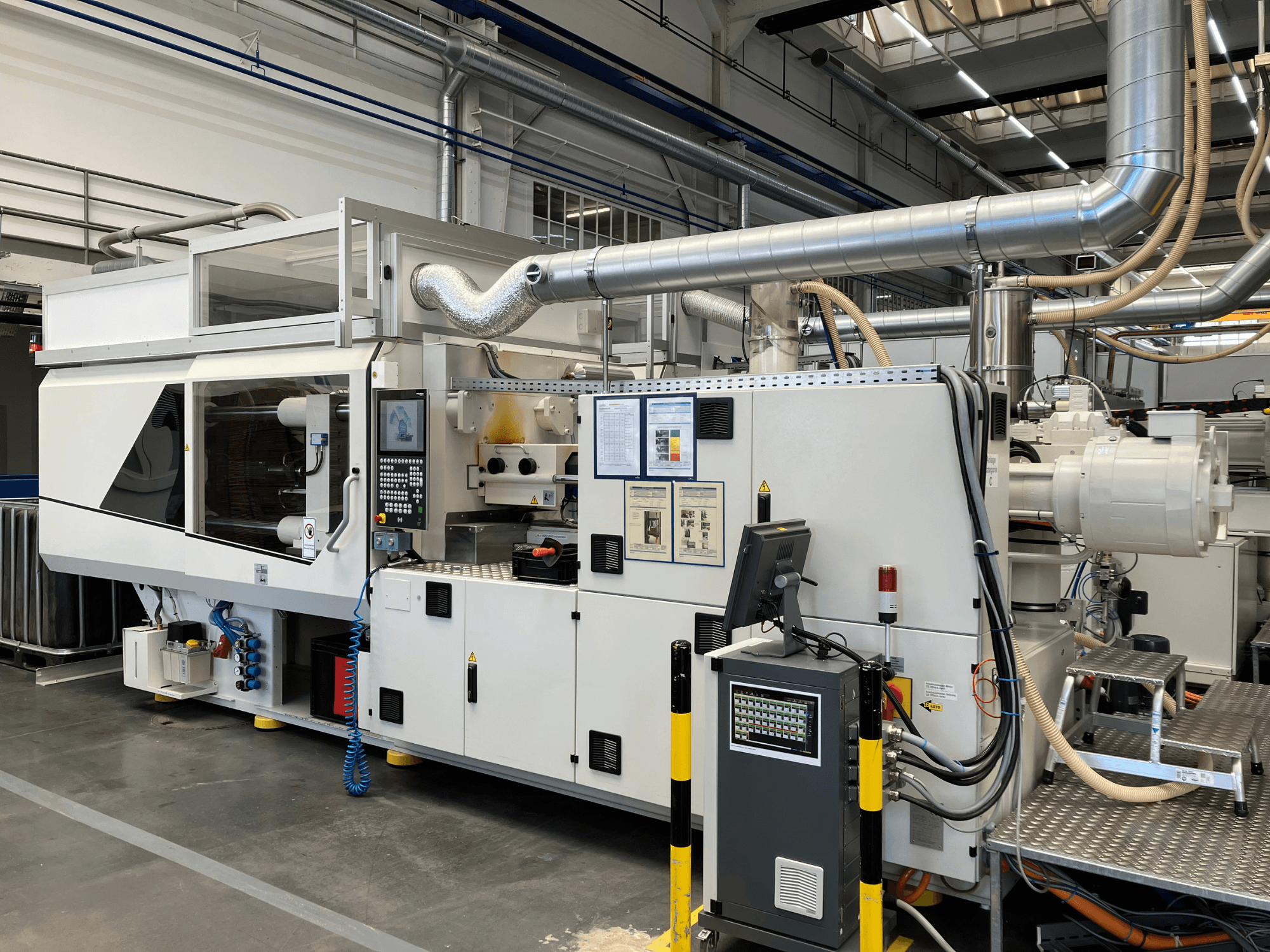 Вид спереду промислової машини з панеллю керування, трубами та екранами дисплеїв, що вирізняється витонченим білим дизайном і технічними деталями.