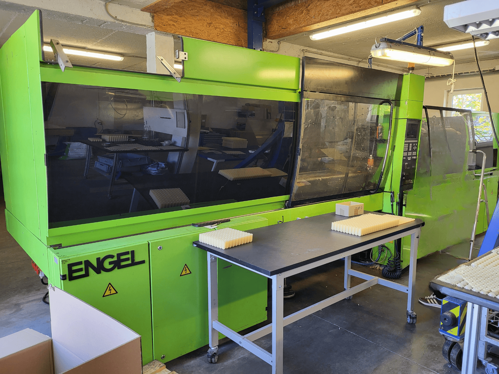 Гідравлічна термопластавтомат Green Engel ES1800/300HL, вид спереду, з матеріалами, складеними на робочому столі.