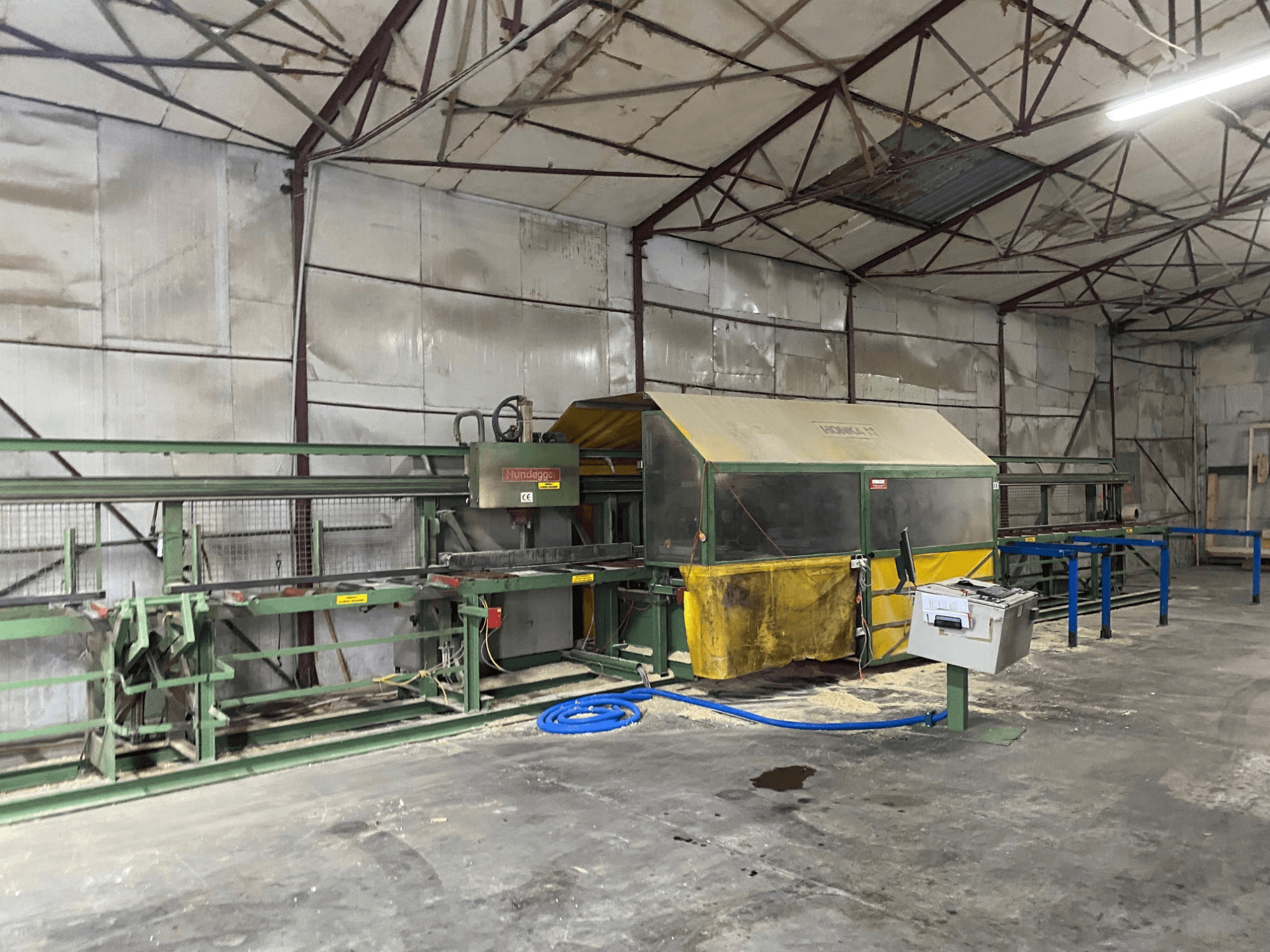 Деревообробний центр з ЧПК HUNDEGGER K1 в майстерні, вид збоку: видно обладнання, елементи керування та тирсу на підлозі.