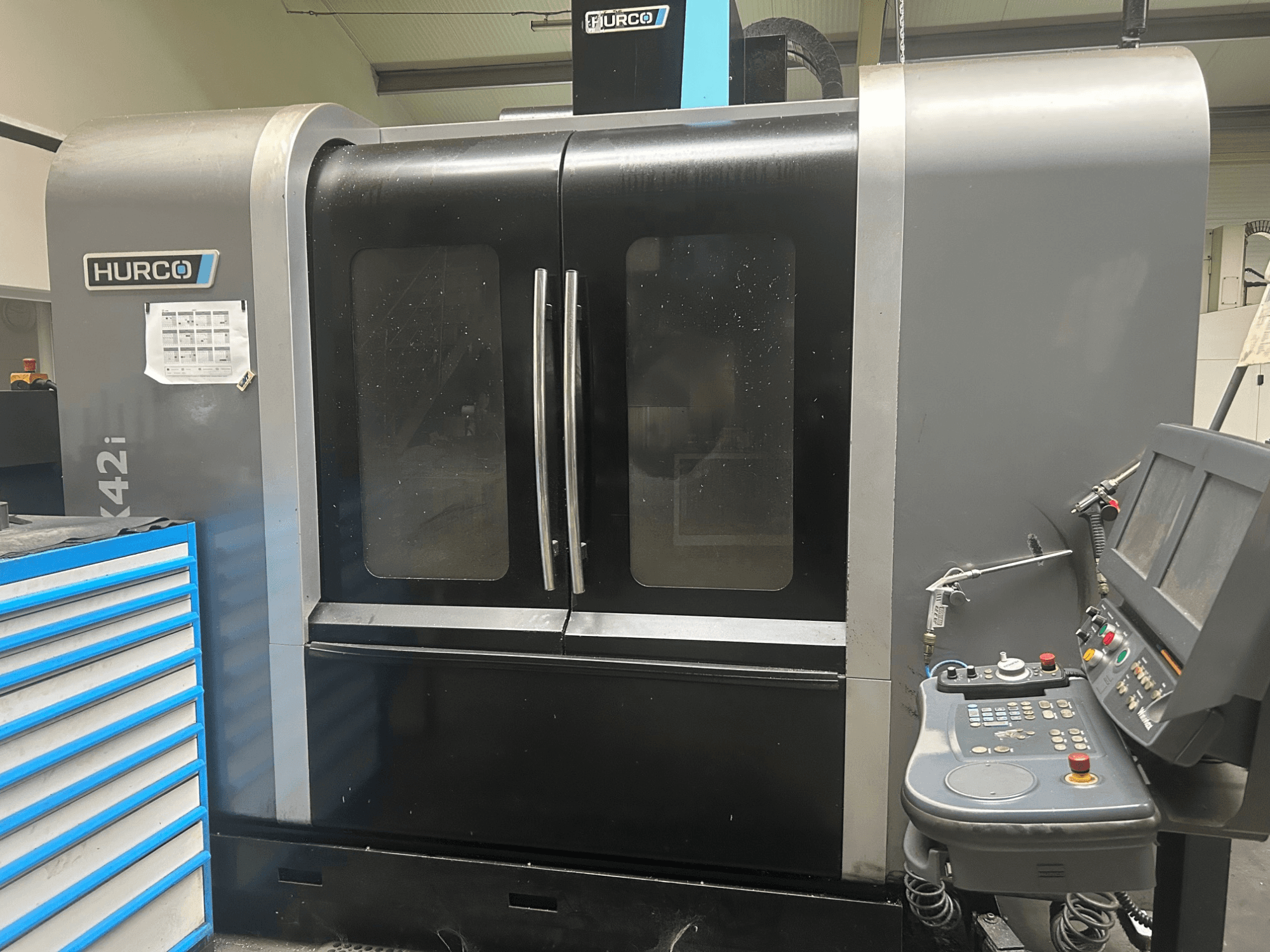 Верстат з ЧПК Hurco VMX42i, вид спереду з панеллю керування збоку, з подвійними дверима і видимими технічними деталями.