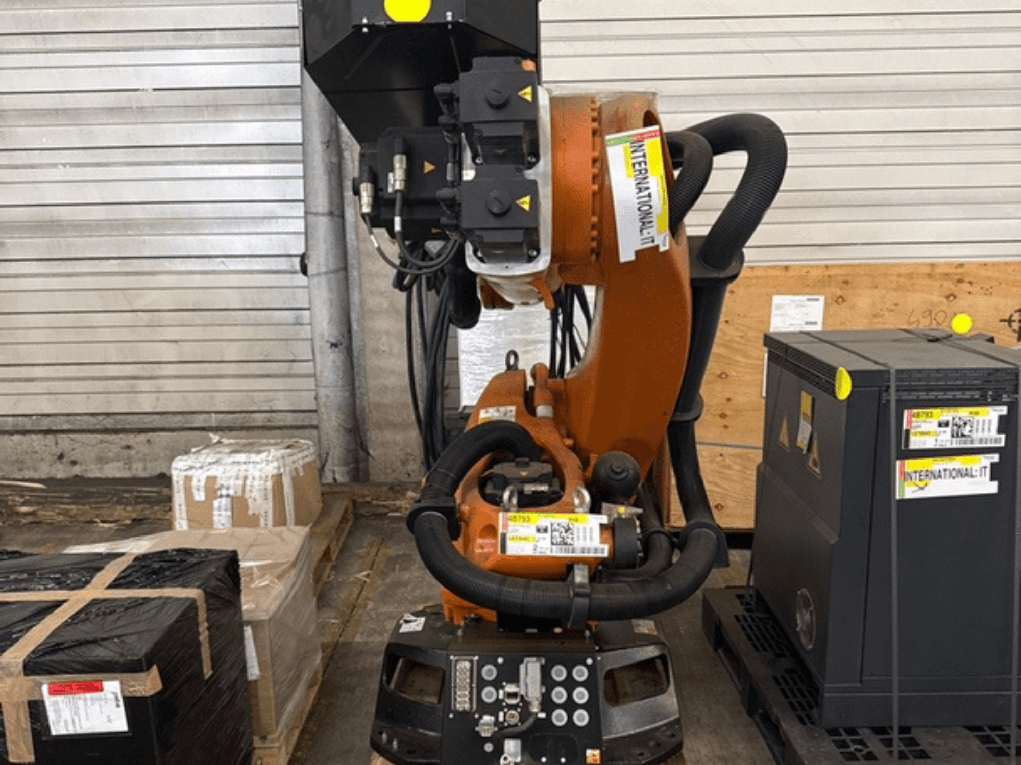 Додатковий маніпулятор робота KUKA KR 210 R2700 у фронтальному ракурсі, розміщений на піддоні поруч із пакунками та обладнанням.