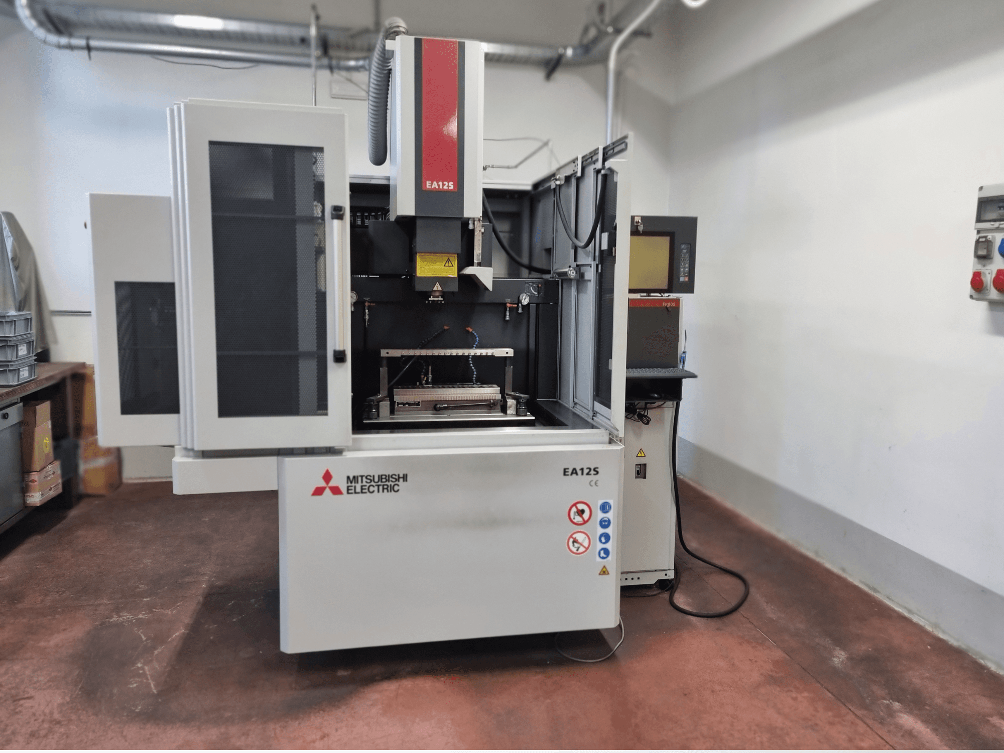 Машина для різання дроту Mitsubishi Electric EA12S, вид спереду, з відкритими дверима, панеллю керування та етикетками безпеки.