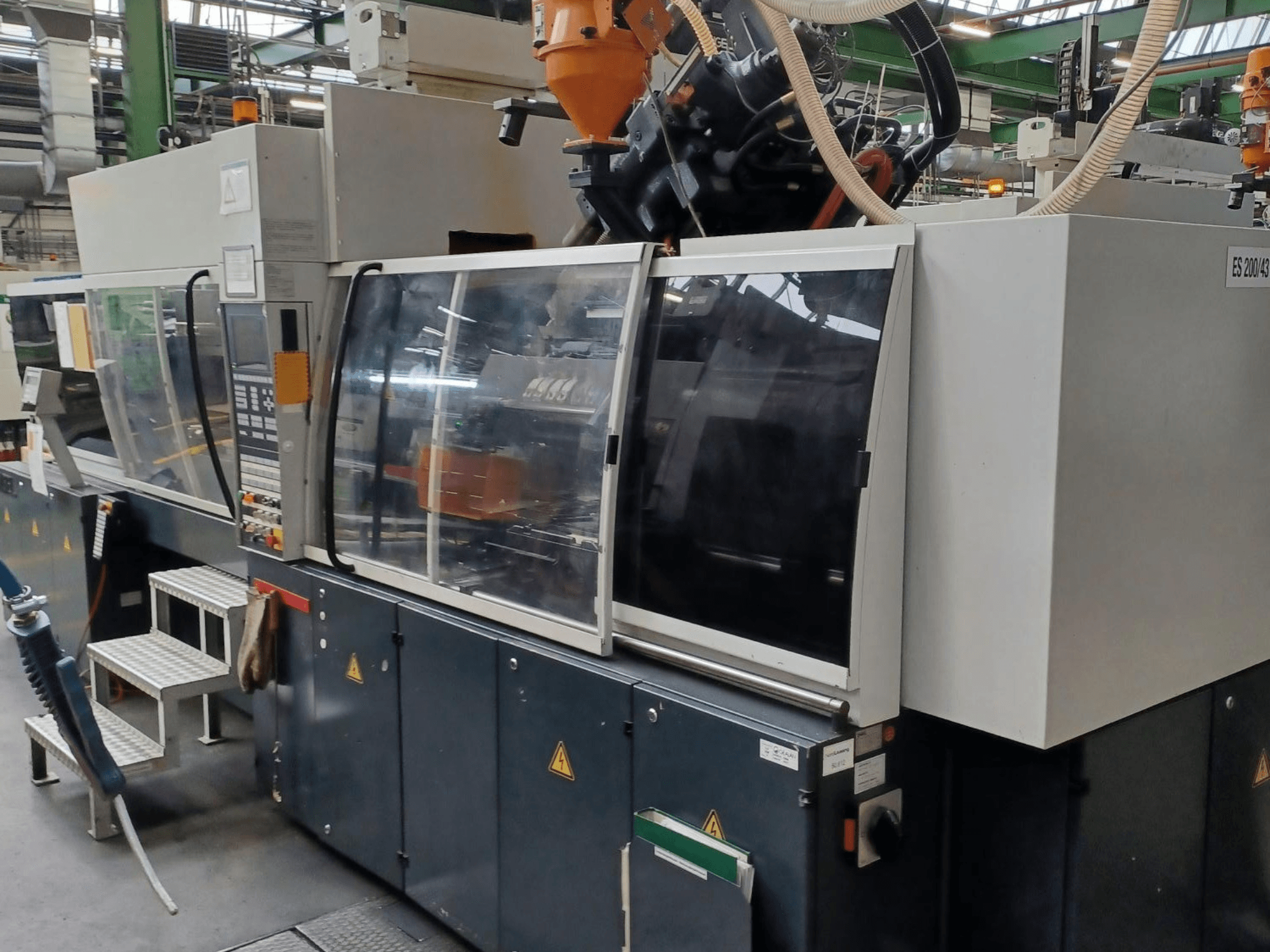 Вид спереду машини для лиття пластмас під тиском, марка і модель невідомі, з прозорими захисними дверцятами і панеллю керування.