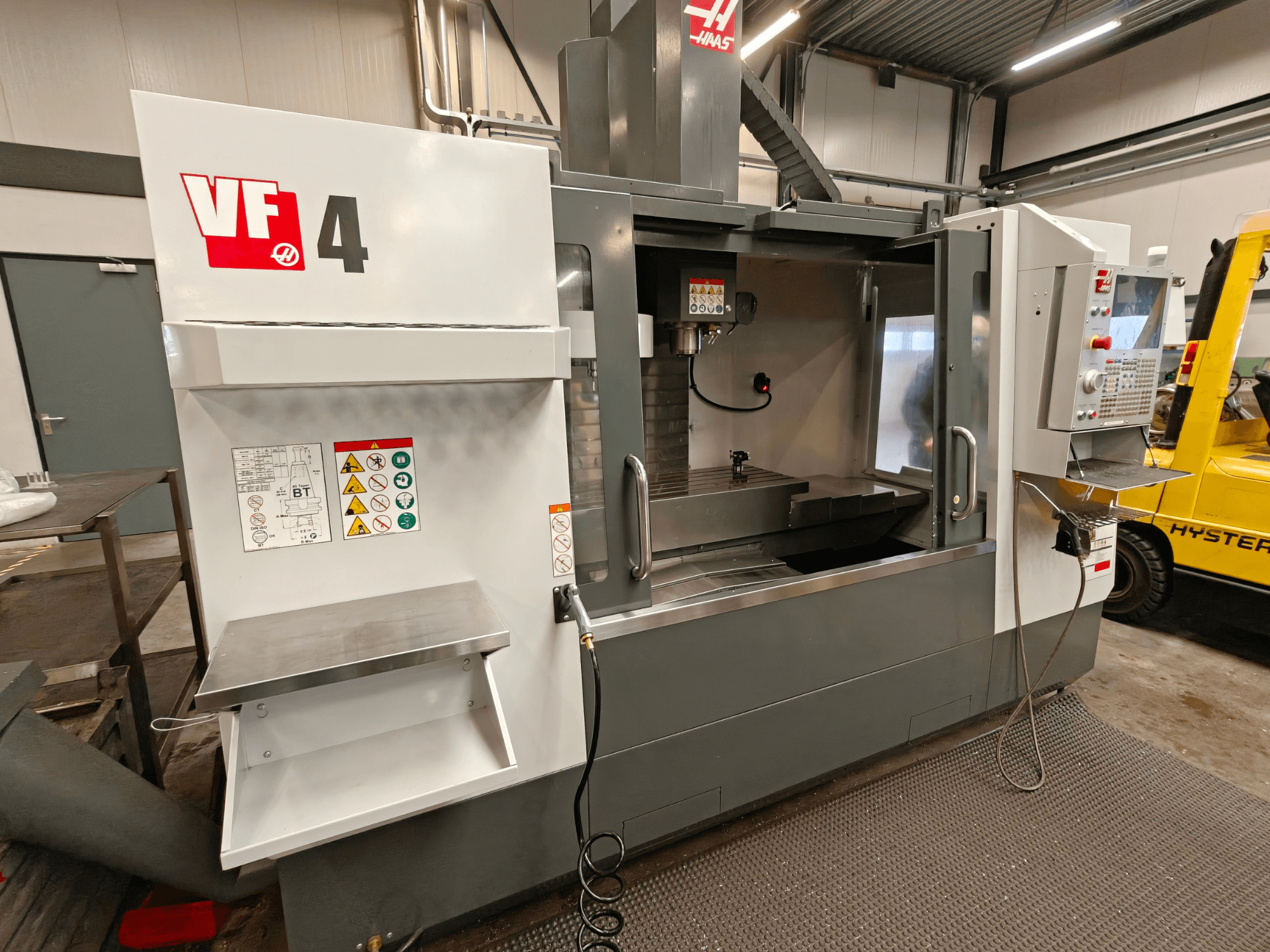 Вертикальний обробний центр HAAS VF-4, вид спереду, з панеллю керування, робочою зоною та етикетками безпеки збоку.