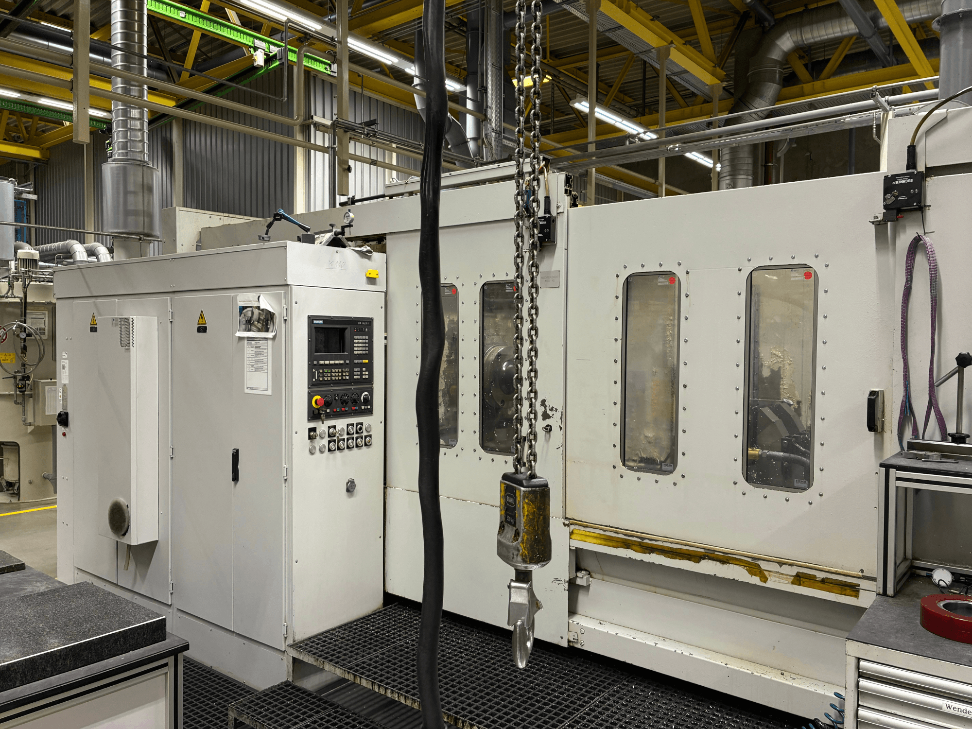 Промисловий верстат з ЧПУ з панеллю керування, вид збоку; має вікна, ланцюги та металеві компоненти в заводському виконанні.