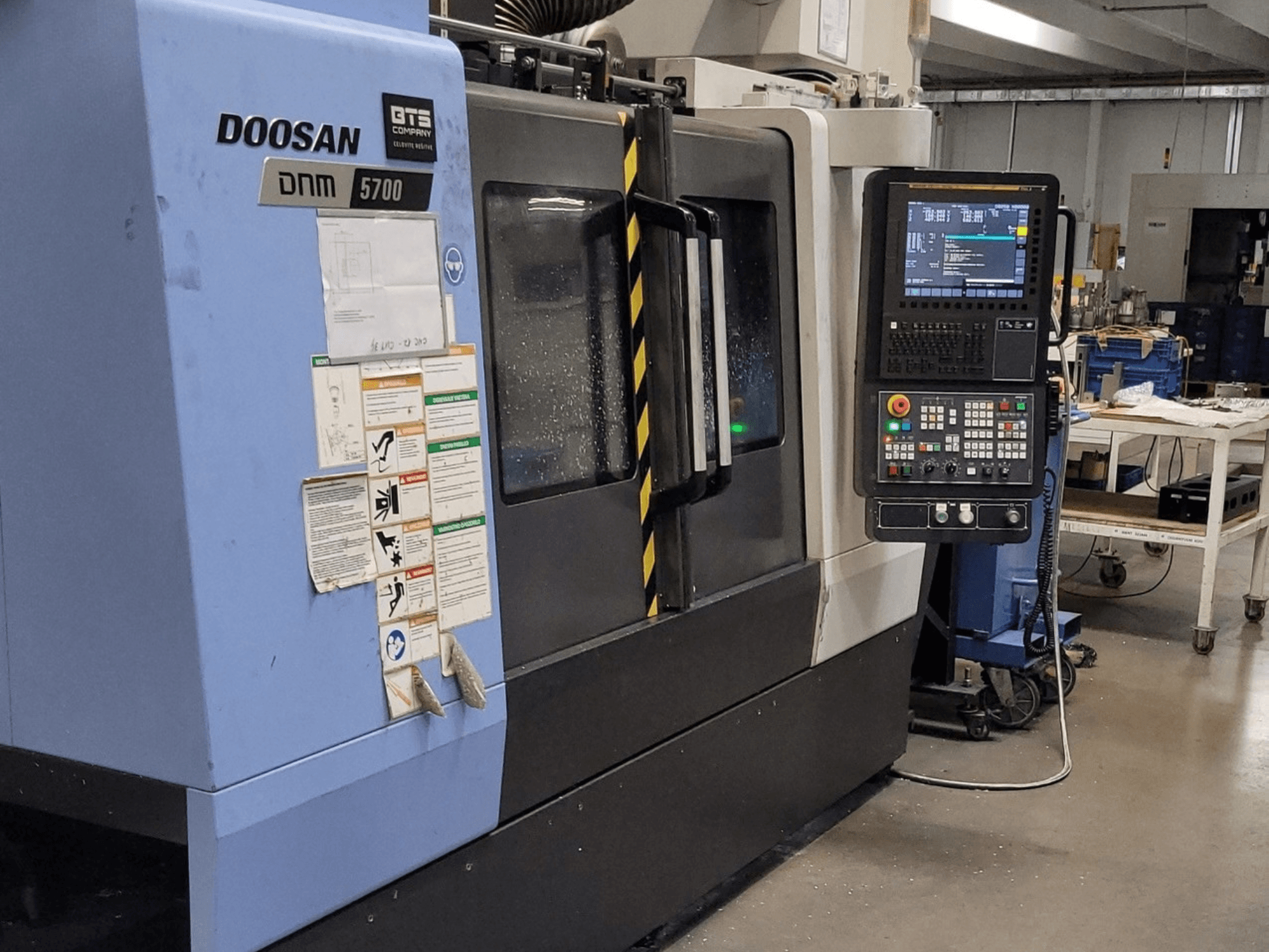 Вертикальний обробний центр DOOSAN DNM 5700, вид спереду, на якому видно панель управління та органи керування.